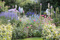 Blühender Garten mit blauer Veronica, Fingerhut und Lerchensporn, dazwischen Gartendeko