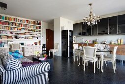 Everything in one room - eclectic dining area in front of modern kitchen counter, large bookcase and striped, country-house sofa