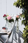 Bottles of flowers hanging on garden chair against white wooden wall