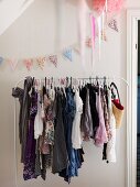 White clothes rail holding girl's clothing and pastel bunting hung on wall