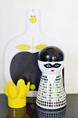 Whimsical salt shaker and yellow, plastic egg cup in front of painted chopping board