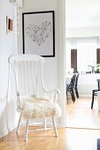 White wooden chair with high backrest and fur cushion in corner; view into dining room through open door to one side