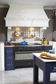 Gas cooker flanked by blue-painted drawer units below masonry mantel hood