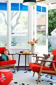 Orangefarbene Sitzgruppe mit Retro Klassikermöbeln vor Erkerverglasung und Gartenblick