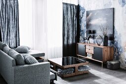 Graumeliert bezogene Couch und Tisch aus Walnussholz mit Ablagefächer, an Wand Sideboard