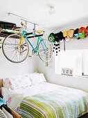 Racing bicycle hung from shelf above bed in teenager's bedroom with collection of peaked hats on wall