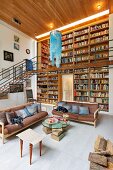 Sofas and side table in front of double-height bookcases with airy steel and wood gallery