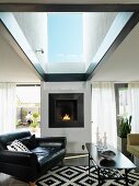 Black leather armchair and coffee table in front of fireplace in living room with large skylight