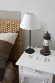 Minimalistische Tischleuchte mit weißem Schirm auf weiss lackiertem Nachttisch, mit Schablonenschrift bedruckt, neben Bett