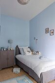 Einzelbett mit grauer Husse und weisser Bettwäsche, neben Retro Metall Schränkchen in Kinderzimmerecke mit hellblauen Wänden