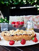 Home-made berry cake with crumble topping and fresh strawberries on cake plate on table outdoors