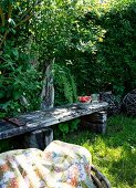 Shady seating area in garden with weathered wooden bench and patterned picnic blanket in foreground