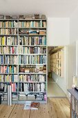Floor-to-ceiling metal bookcase next to open doorway with view of wooden wall-mounted shelves in hallway