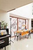Open-plan interior; dining area with orange tablecloth, roller blinds on windows and black upright piano