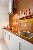 Kitchen counter with white base unit, exotic wood worksurfaces and back wall, cylindrical extractor hood with LED lights