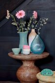 Pink gerbera daisies in various vases and pastel bowls on round stone table