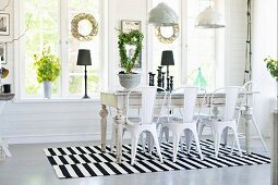 Retro metal chairs around rustic dining table on black and white striped rug below pendant lamps in dining room with wreaths on windows
