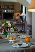 Set table with pastries under glass cover, vase of flowers and glass carafe of juice