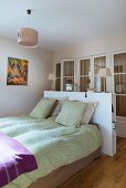Lime green bed linen and pillows on bed below table lamps on white, modern half-height partition in front of fitted wardrobes with lattice doors