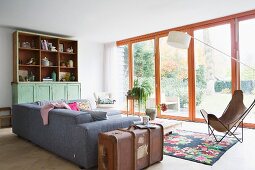 Graues Polstersofa, seitlich Vintage Koffer und Butterfly-Sessel in Wohnzimmer mit Terrassentüren