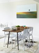 Schlichter Esstisch mit weissen Stühlen auf hellem Kuhfellteppich, moderne Landschaftsgemälde an der Wand