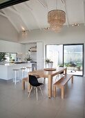 Open-plan kitchen-dining area with island counter and wooden table below exposed beams in open roof area
