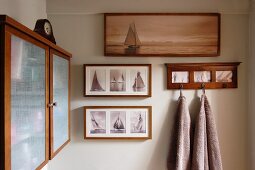 Framed photos of sailing ships and towels hanging from wall hooks; wooden wall cabinet with opaque glass doors to one side