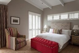 Klassisches Schlafzimmer mit Sichtbalkendecke, gepolsterter Betttruhe und einem gestreiften Sessel