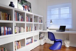 Violet, retro, plastic shell chair at desk below window with closed roller blind; white bookcase with drawer elements to one side