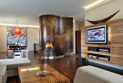 Integrated interior design in open-plan living-dining room; matching wood structure on media wall and coffee table; fireplace in curved wall element in background