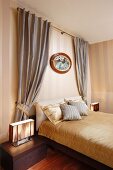 Bett mit goldfarbener Bettwäsche, vor Wand mit Streifenmuster Tapete und drapierter Vorhang in elegantem traditionellem Schlafzimmer