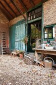 Gardening utensils on gravel floor in front of brick façade of old farmhouse with turquoise barn doors and industrial windows