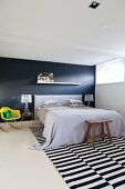 Doppelbett vor schwarzer Wand, schwarz-weiss gestreifter Teppich auf hellem Boden