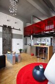 Wohnraum im Loftstil, offene Küche unter Galerie mit roter Glasbrüstung, im Vordergrund roter Teppich mit Beistelltisch