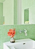 Bathroom with green mosaic tiles and vase of flowers on sink