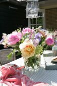 Blumenstrauss mit Pfingstrosen und Anemonen in Glasvase auf Terrassentisch