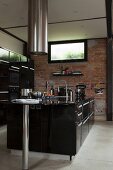Schwarze, freistehende Designer-Küchentheke unter zylindrischem Edelstahl Dunstabzug vor Ziegelwand