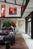 Grey sofas in lounge area and dining area with graffiti-style artwork on wall below encircling gallery in loft apartment