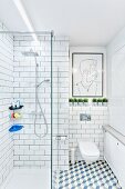 White, modern bathroom with tiled walls & floor, glazed, floor-level shower and modern artwork above wall-mounted toilet
