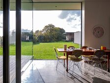 Classic wire-framed chairs around wooden dining table with place settings in front of glass wall with garden view