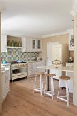 White fitted kitchen with mosaic splashback, retro cooker, retro fridge, breakfast bar & bar stools