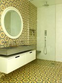 Waschtisch und runder Wandspiegel neben bodenebener Dusche mit Glas Trennscheibe im Badezimmer mit Retro Fliesen