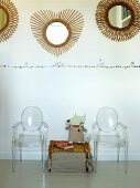Truhe aus Geflecht zwischen Ghost Stühlen, oberhalb runde Spiegel mit strahlenförmigem Rahmen an Wand