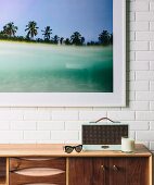 Sideboard with retro utensils against a white brick wall and a framed color photo
