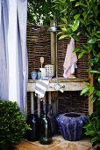 Improvised shower area in garden with wicker hurdle screen and blue planters on floor