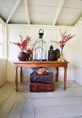 Candle lantern and vessels with branches on tropical wooden table, vintage suitcase on the white patinated wooden floor