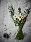 Weiß blühender Blumenstrauss mit schwarzweisser Dekoschnur auf Papier mit Knitterstruktur