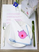 A summer place setting – a fabric napkin with a teapot motif and a lantern on a piece of paper with a poem