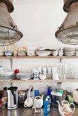 Detail of kitchen; crockery on wooden shelves, utensils on stainless steel worksurface and industrial-style pendant lamps