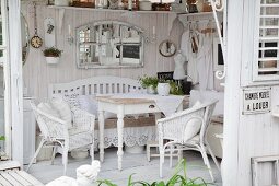 Wooden table and white wicker chairs in shabby-chic summer house with white wooden floor